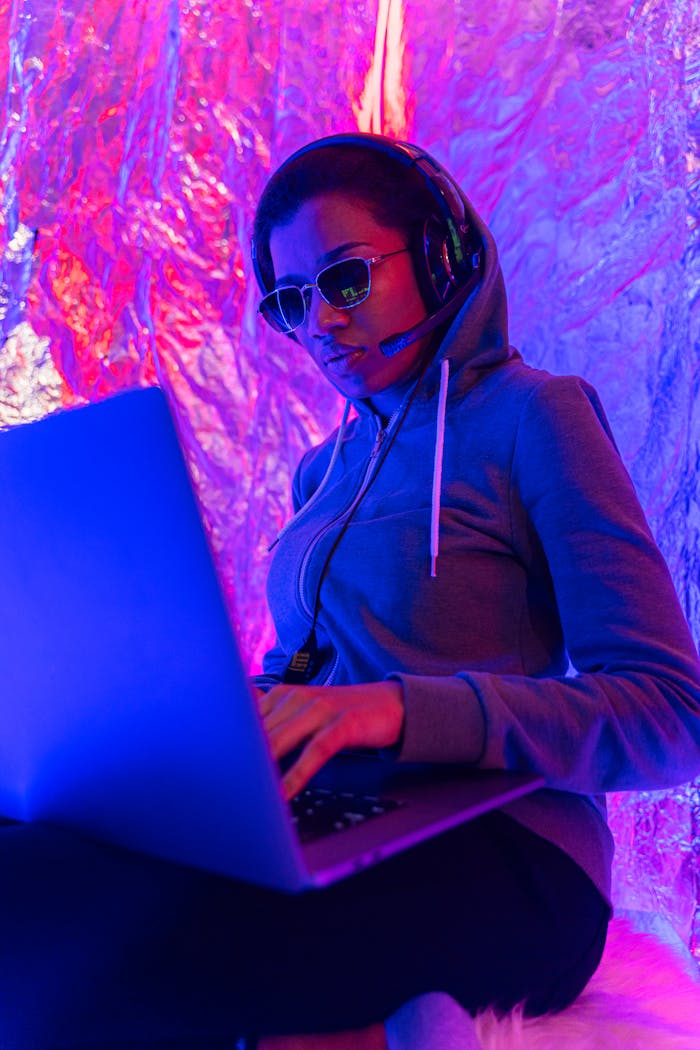 Home Woman in hoodie and headphones engaging with a laptop in a vibrant, futuristic setting.
