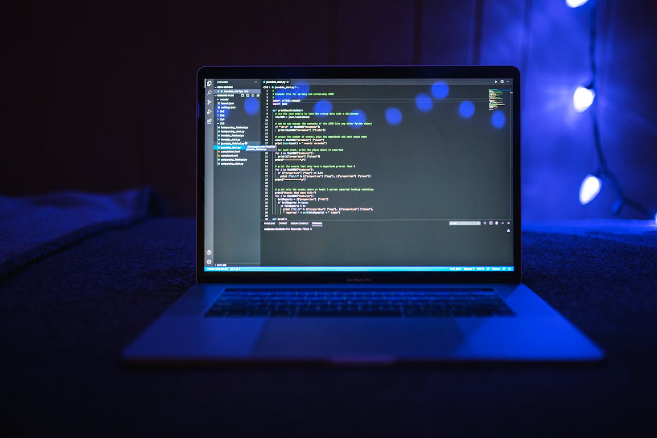 Home Close-up of a laptop screen displaying code, set against a dark backdrop with blue lighting for a tech-focused ambiance.
