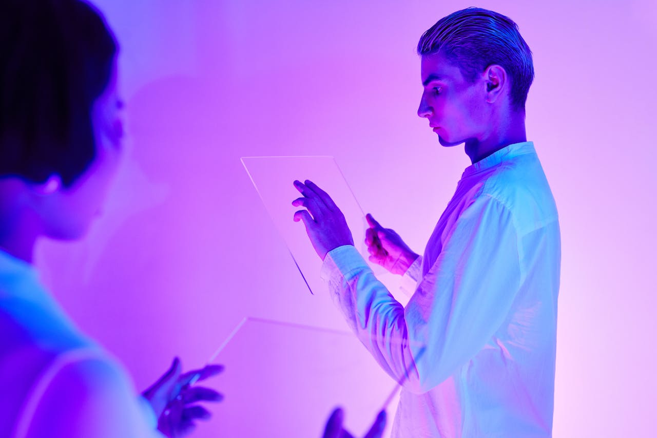 Home Two individuals engaging with futuristic transparent touch screens in a vibrant purple-lit studio.